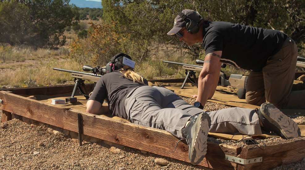 Person shooting scoped rifle facing left