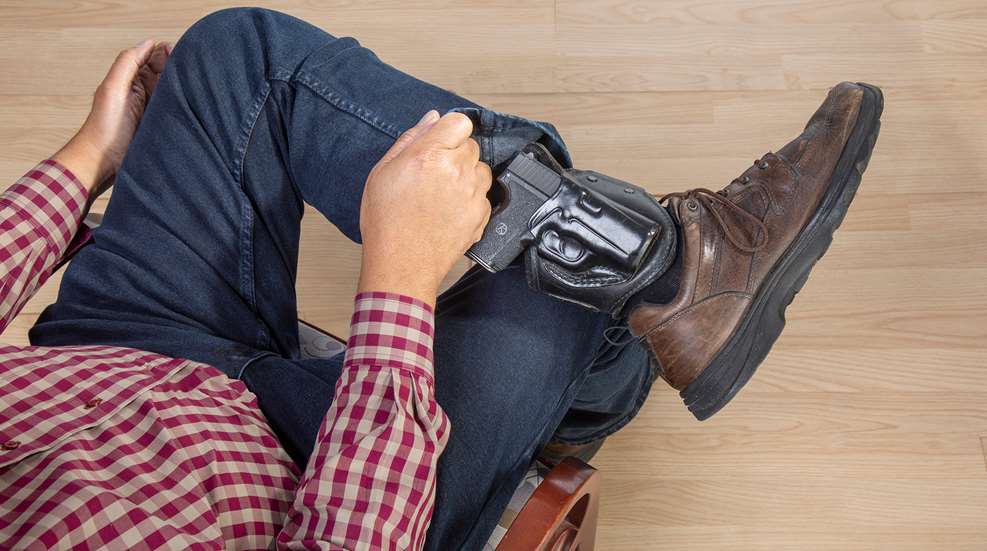 person seated with an ankle holster and handgun