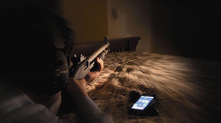 man aiming shotgun at bedroom door in the dark