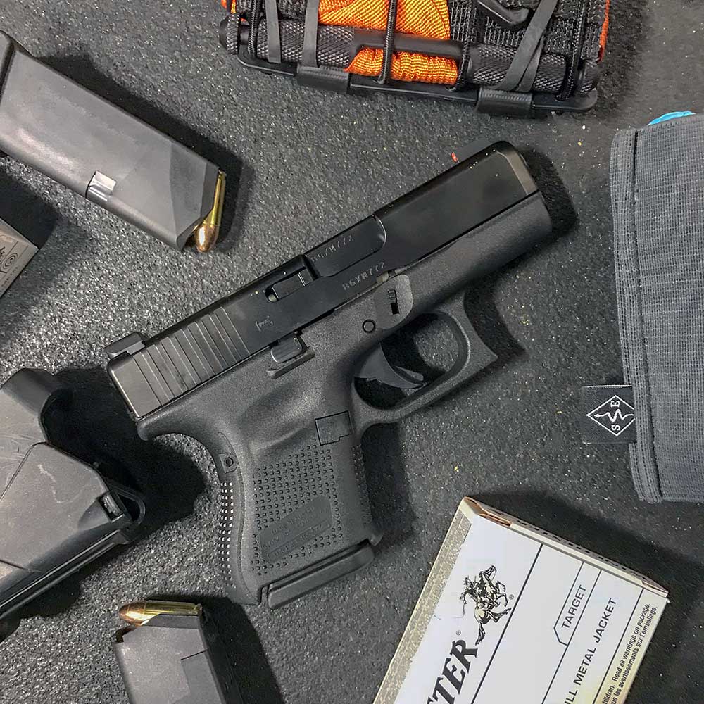 Glock 26 Gen 5 on a black background surrounded by loaded magazines, a box of ammo and a tourniquet.
